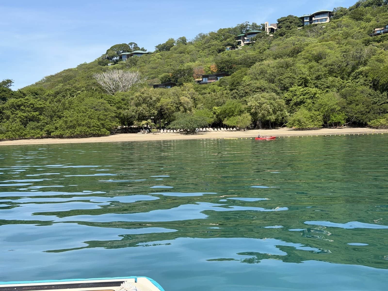 Turquoise water off Playa Nacascolo with a red kayak near the shore and villas tucked into the forested hillside
