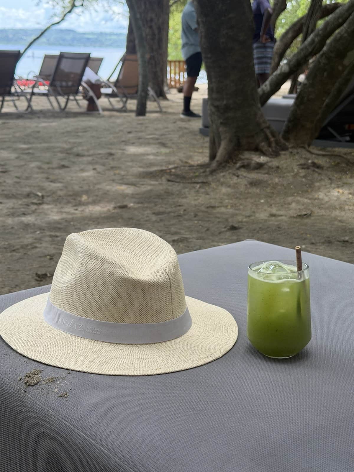 A green cucumber margarita and a straw hat on a beach daybed table at Casa de Playa