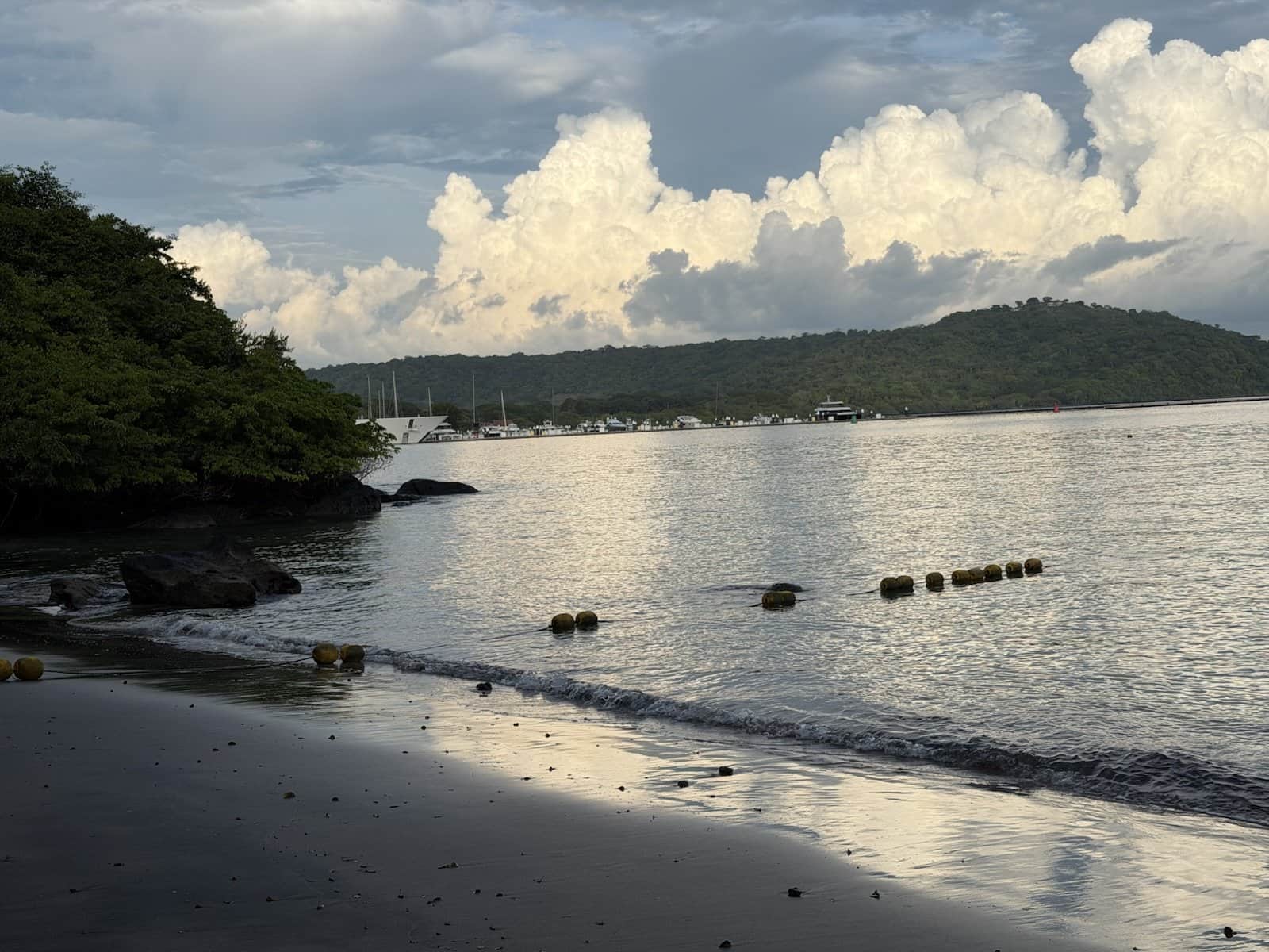 Dark wet sand at Playa Sombrero Oscuro reflecting the sky, a line of buoys and towering clouds over Culebra Bay