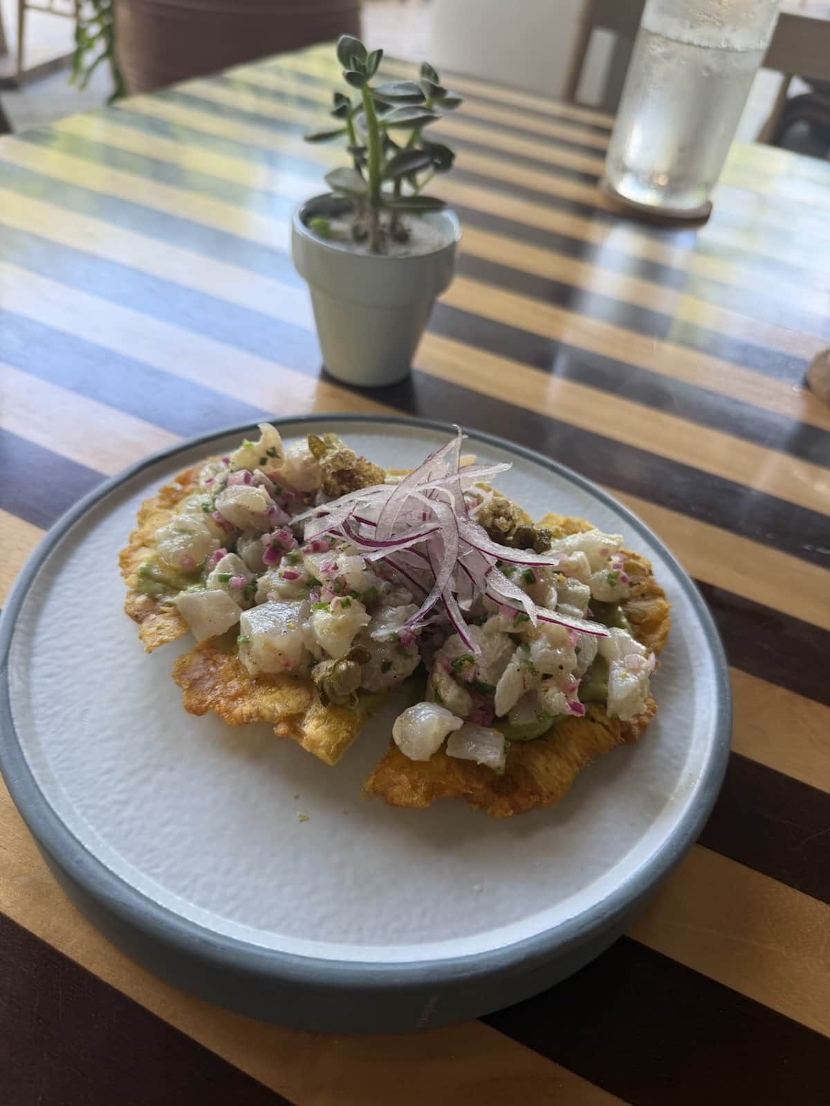 A toston topped with Sicilian crudo, red onion and herbs on a grey plate at Meso